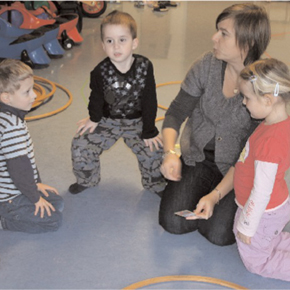 3 Kinder und eine Betreuerin am Boden im Kreis sitzend